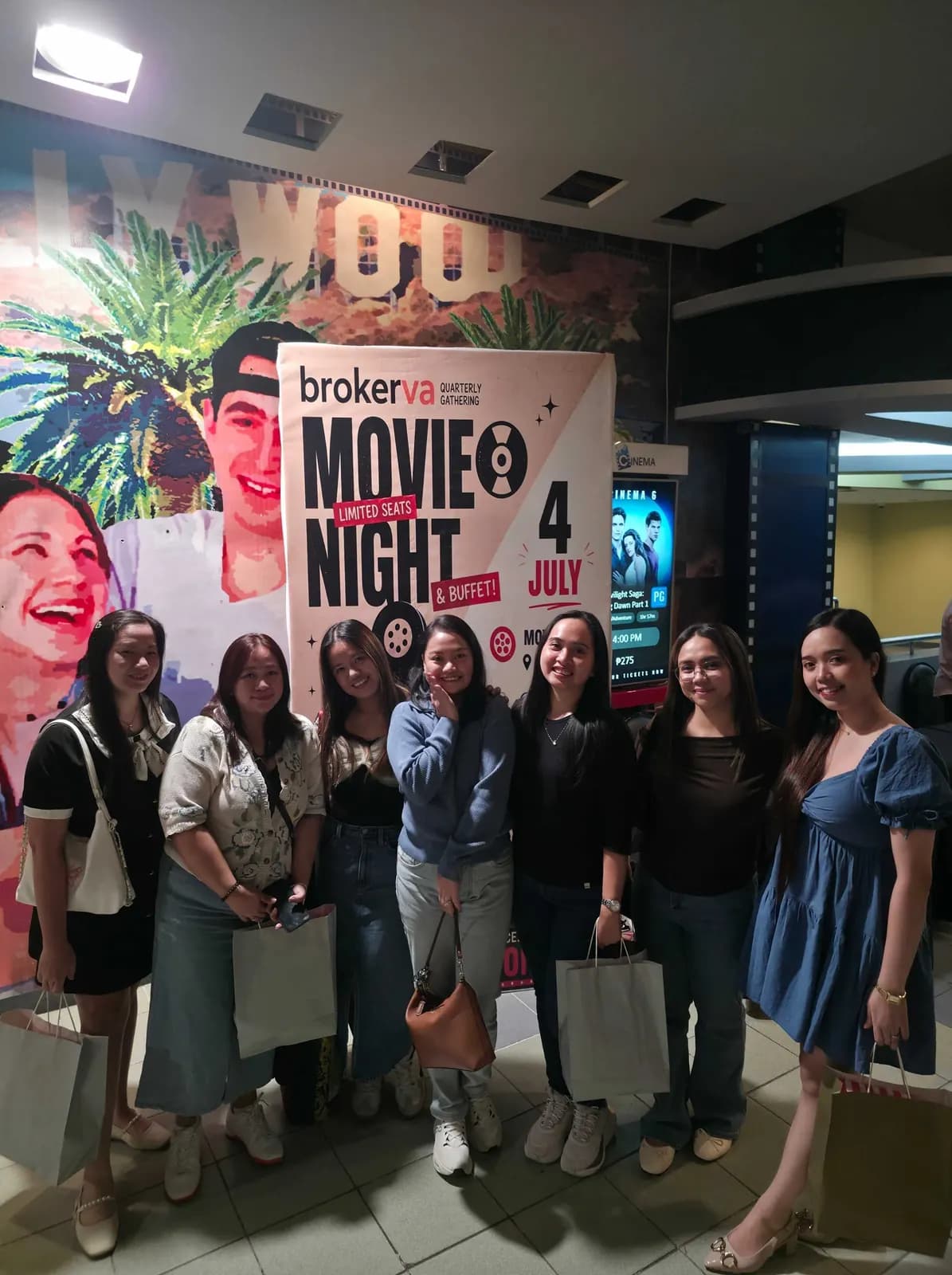 Teammates with their gift bags beside the BrokerVA Movie Night standee, July 2026